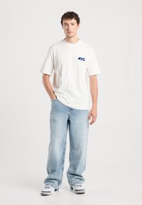 White short-sleeve t-shirt with blue "NYC" graphic on the chest, paired with light blue wide-leg jeans and white sneakers with gray accents.