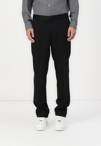 Svarta byxor med rak skärning, strukturerad tygkvalitet och knappstängning, kombinerat med vita sneakers och en grå skjorta med knappar.