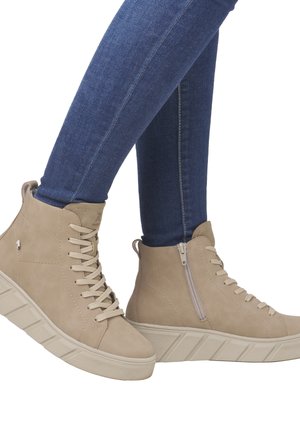 Beige High-Top-Stiefel mit Schnürung und seitlichem Reißverschluss, mit einer strukturierten Wildleder-Oberfläche und einer dicken, geriffelten Gummisole. Die Jeans sind dunkelblau.