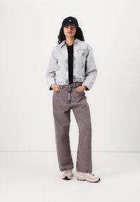 Lys grå, cropped denimjakke over en svart skjorte, kombinert med løse, lys lilla jeans og beige sneakers. Svart caps gir et ekstra detalj.