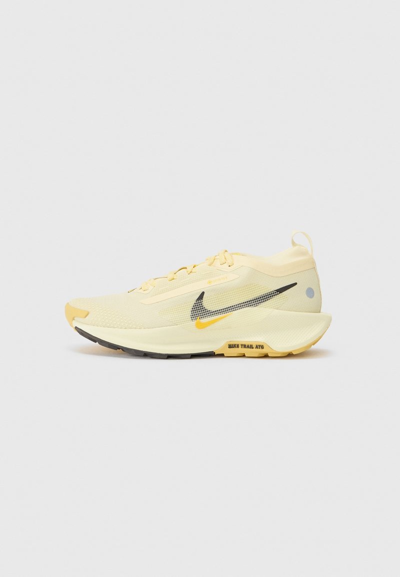 Chaussure de course jaune clair avec le swoosh Nike noir et jaune, semelle texturée et texte "NIKE TRAIL ATG" sur fond blanc.