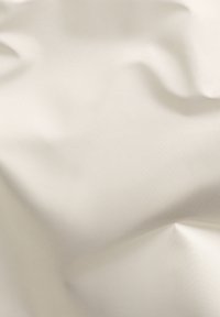 Cremefarbener Stoff mit glatter Textur, der sanfte Falten und einen subtilen Glanz zeigt. Keine auffälligen Muster oder Hardware sichtbar.