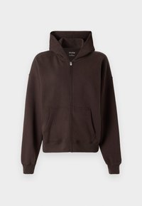 Smeđa zip-up zipica izrađena od mekog materijala. Ima veliki kapuljaču, prednje džepove i rebraste manžete i rub. Jednostavan, ležeran dizajn.