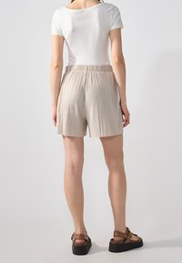 Krémové skládací šortky s elastickým pasem, vyrobené z lehké látky. V kombinaci s upnutým bílým tričkem a hnědými sandály na platformě.