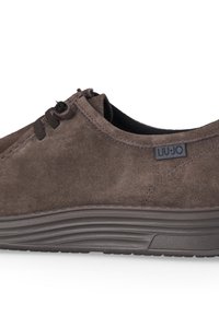 Scarpe in camoscio marrone con profilo basso, design con lacci, superficie testurizzata e suola in gomma spessa e scanalata. Presenta una toppa con logo di marca.