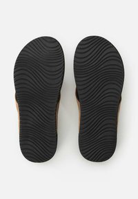 Sorte gummisåler med et bølget dækmønster, der viser en brun fodseng og sidedele. Glat overflade uden fremtrædende hardware.