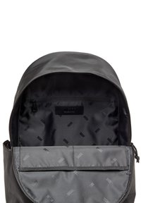 Sac à dos noir avec un extérieur lisse et mat, doté d'un dessus zippé. Intérieur doublé de tissu gris affichant le logo "DIESEL" dans un motif répétitif.
