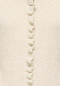 Tissu en maille crème douce avec une rangée verticale de petits boutons transparents, chacun encadré par un bord délicatement froncé.