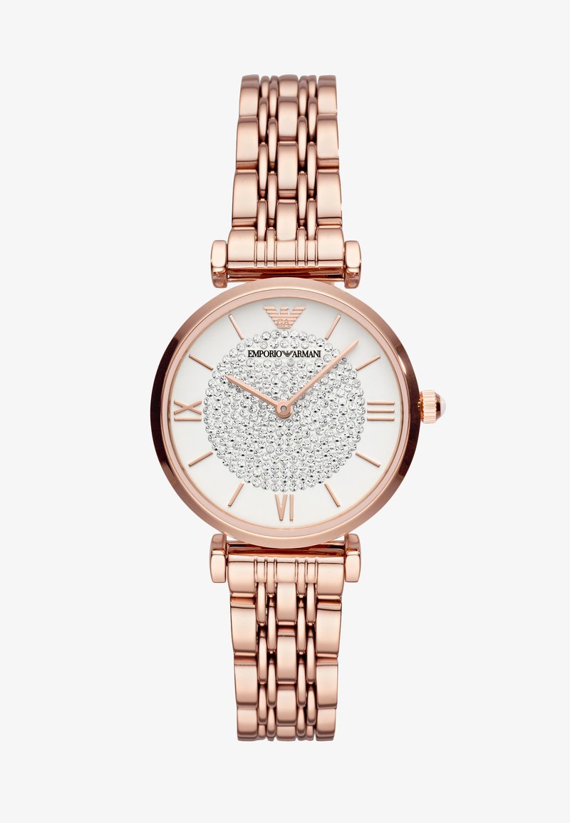 Okrągły zegarek z różowo-złotą metalową bransoletą i fakturowaną białą tarczą, z okręgiem ozdobionym kryształami oraz znacznikami w postaci cyfr rzymskich.