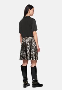 Schwarzes kurzärmliges Hemd, gemusterter plissierter Rock mit schwarz und Tierdruck sowie knielange glänzende schwarze Stiefel mit Kettendetails.