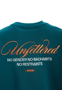 Sudadera en color azulado con texto bordado. "Sin ataduras" en cursiva naranja, seguido de texto blanco: "SIN GÉNERO SIN MALOS HÁBITOS SIN RESTRICCIONES".