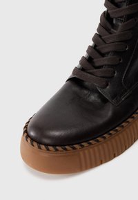 Bottine en cuir noir avec orteil arrondi, semelle en caoutchouc texturée, détails brodés marron et lacets assortis marron.