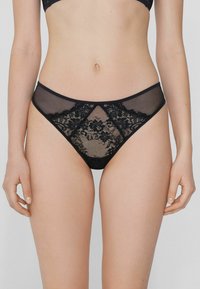 Culottes de bikini en dentelle noire avec des panneaux en maille transparente, des motifs floraux et une coupe taille basse avec une ceinture et des finitions lisses.