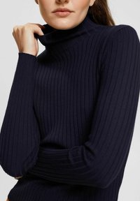 Marineblauer Rippenrollkragenpullover mit langen Ärmeln, eng anliegendem Design und durchgehend strukturiertem Muster.