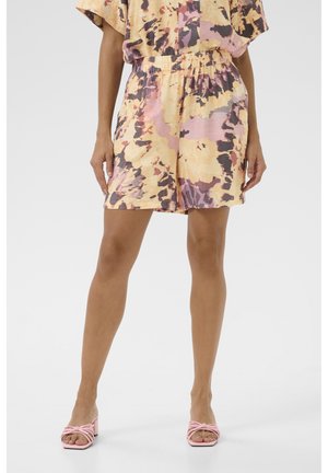 Floral tie-dye shorts in pastelgeel, roze en paars met een elastische tailleband. Gecombineerd met roze hakken met bandjes.