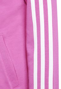 Sudadera rosa con una textura suave, con rayas blancas a lo largo de las mangas y un bolsillo canguro en la parte frontal.