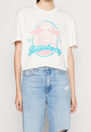 Biały T-shirt z krótkim rękawem z niebieskim i różowym logo Billabong oraz wzorem palmy, noszony z jasnoniebieskimi podartymi dżinsami.