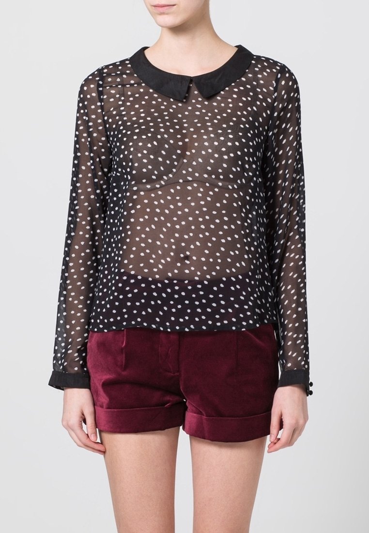 Blusa negra transparente con lunares blancos, cuello redondeado, mangas largas y puños, combinada con pantalones cortos de terciopelo burdeos.