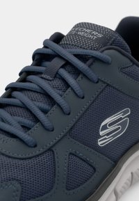 Dark blue athletic shoe with mesh fabric, textured accents, flat laces, and a silver logo. Features padded tongue and lightweight sole.