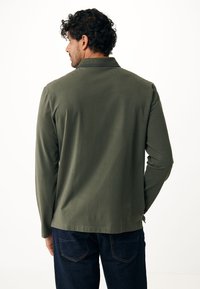 Olijfgroene langemouwen shirt met een kraag, met een gladde textuur en rechte zoom, gecombineerd met donkerblauwe denim broek.