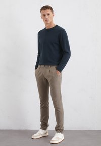 Marineblaues Langarmshirt, kombiniert mit beigefarbenen, gefalteten Hosen und weißen Sneakers. Glattes Material, taillierte Passform und subtile Details sind sichtbar.