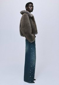Chaqueta corta de piel sintética en marrón claro, combinada con jeans de mezclilla azul de cintura alta que tienen brillantes dispersos en la parte inferior.