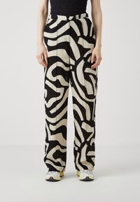 Zwart-witte, gemarmerde, wijde broek met een gladde textuur, hoge taille en opvallend abstract ontwerp. Gecombineerd met witte en gele sneakers.