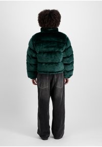 Jachetă puffer din blană artificială verde, cu secțiuni matlasate orizontale, guler înalt și croială lejeră. Potrivită cu blugi negri, largi.