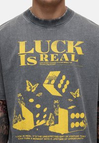 Szara bawełniana koszulka z żółtym napisem graficznym "SZCZĘŚCIE JEST RZECZYWISTE" oraz wzorami kostek, motyli i kwiatów. Styl z okrągłym dekoltem.