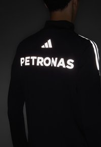 Sort langærmet top med reflekterende "PETRONAS" og adidas-logo på ryggen, med hvide lodrette striber langs skuldrene.