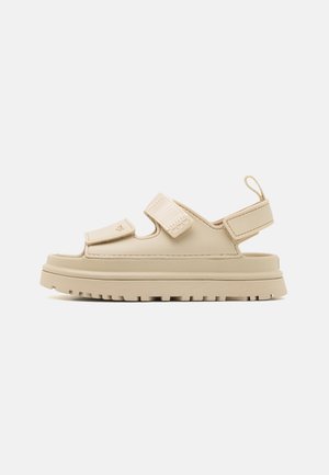 Beige sandal med två justerbara kardborreband, öppen tådesign, tjock vadderad sula och en texturerad yttersula för bra grepp.