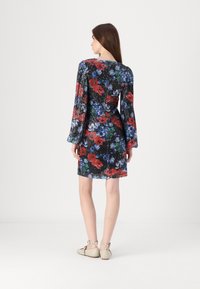 Robe noire à motifs floraux avec un tissu plissé, de longues manches évasées et des motifs floraux rouges et bleus éclatants. Vue de dos, associée à des chaussures beiges.