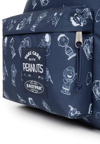 Námořnický modrý batoh s bílými kreslenými postavičkami, přední kapsou s nápisem "Pečuji s Buráky" a logy "EASTPAK", a detailem na zipu.