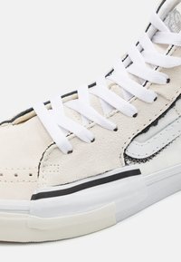 Hvide ruskinds højtop sneakers med sorte accenter, hvide snørebånd og tekstureret overflade. Har et markant side-swoosh logo.