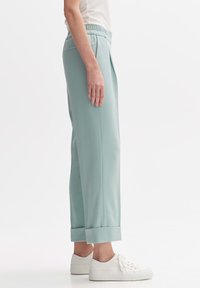 Joggers vert menthe au fit décontracté, avec une taille élastique et des poignets repliés, associés à des baskets blanches. Texture du tissu lisse.