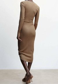 Abito bodycon in maglia beige con maniche lunghe, lunghezza al polpaccio, presenta una texture a coste e una silhouette aderente, abbinato a tacchi a piattaforma nudi.