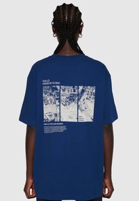 Marinblå oversized t-shirt i bomull med ett grafiskt tryck på ryggen som har vit text och bilder av fågelperspektiv.