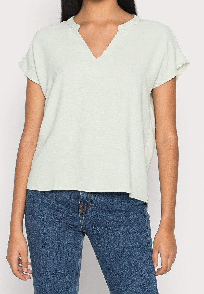 Maglietta verde chiaro a maniche corte con scollatura a V, vestibilità rilassata e texture liscia. Abbinata a jeans blu scuro.