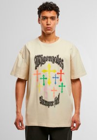 Camiseta de gran tamaño color crema con mangas cortas, que presenta gráficos de cruces coloridos y un texto negro en negrita en el centro y en la parte inferior.