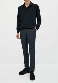 Marineblaues, mit Reißverschluss versehenes Langarm-Pullover kombiniert mit dunkelgrauen, taillierten Hosen und schwarzen Wildlederschuhen. Glatte Textur, figurbetontes Design.