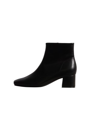 Bota de tobillo de piel negra con tacón bajo de bloque y puntera puntiaguda, vista desde el lado exterior sobre un fondo blanco.