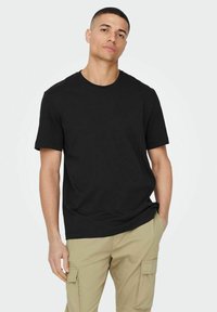 Schwarzes Baumwoll-T-Shirt mit rundem Halsausschnitt und kurzen Ärmeln, kombiniert mit hellen khakifarbenen Cargo-Hosen mit Seitentaschen und einer lockeren Passform.