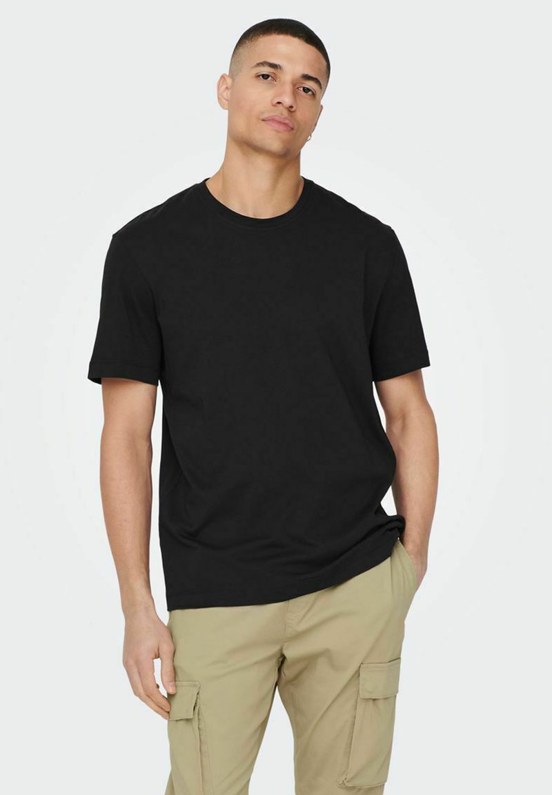 Schwarzes Baumwoll-T-Shirt mit rundem Halsausschnitt und kurzen Ärmeln, kombiniert mit hellen khakifarbenen Cargo-Hosen mit Seitentaschen und einer lockeren Passform.