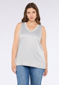 Top senza maniche grigio chiaro con scollatura a V, realizzato in tessuto morbido, caratterizzato da una vestibilità rilassata, abbinato a jeans blu decorati con elementi colorati.