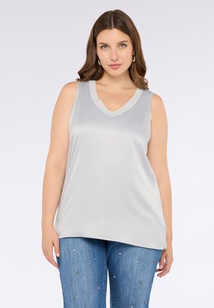 Top senza maniche grigio chiaro con scollatura a V, realizzato in tessuto morbido, caratterizzato da una vestibilità rilassata, abbinato a jeans blu decorati con elementi colorati.