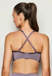 Bra sportivo viola con finitura testurizzata, dotato di spalline incrociate e linee nere di accento. Chiusura regolabile con gancio sul retro.