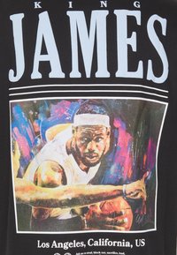 Camiseta negra con una ilustración colorida de un jugador de baloncesto en acción, con un texto blanco en negrita que dice "KING JAMES" arriba.