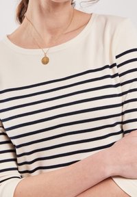 Kräm- och marinblå randig topp med rund halsringning, trekvartslånga ärmar och mjuk textur. En delikat guldhängehalsband bärs.