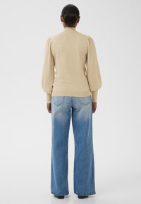 Bež punase kootud sviiter kõrge kraega ja puhuvate pikkade varrukatega, koos laia säärega siniste teksadega, millel on kulunud detail ääres.