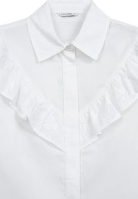 Camicia di cotone bianca con colletto a balze, dettagli di ricamo floreale, chiusura frontale con bottoni e texture liscia.